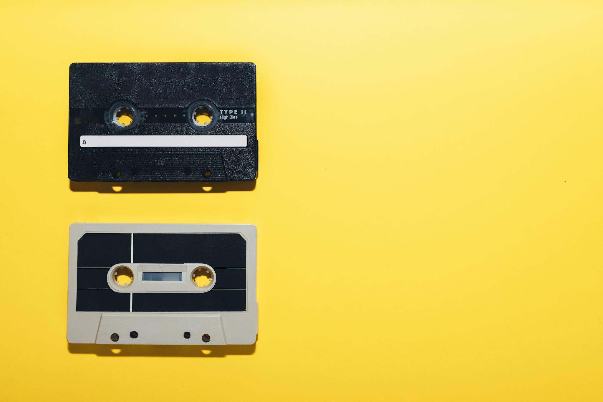 Two vintage cassette tapes on a bright yellow background, capturing a retro and nostalgic vibe.